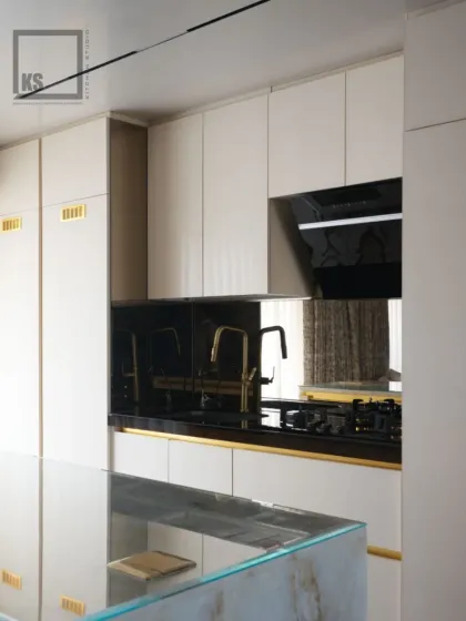 A compact yet luxurious kitchen featuring off-white cabinets with subtle gold accents. The black mirrored backsplash adds depth and a touch of glamour, proving that even smaller spaces can be highly sophisticated.