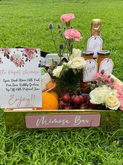 A 'Perfect Mimosa' bar in a box. This hamper includes champagne, fresh juices, and fruits, all beautifully arranged in a golden crate for a celebratory brunch.