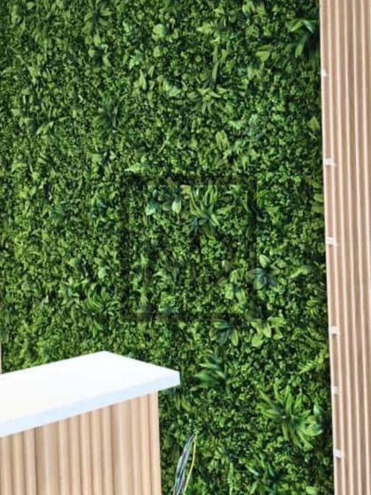 A reception desk area featuring a combination of a dense artificial vertical garden and light-colored fluted wall panels. The contrast between the green texture and the clean lines creates a fresh, modern look.