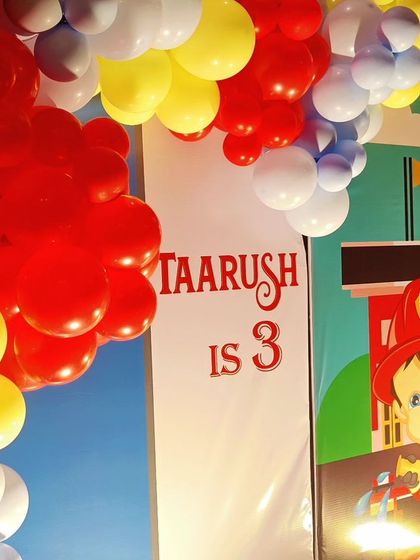 A close-up of a Fireman-themed backdrop, featuring a cartoon firefighter and a 'Taarush is 3' sign.