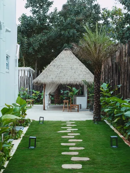 A pathway of stepping stones leads through a manicured lawn to a tranquil thatched-roof gazebo. This showcases my approach to landscape architecture, where every element is designed to create a journey through the space.