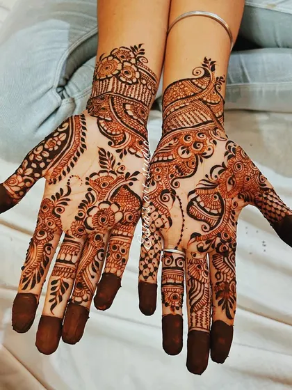 This is a classic Indo-Arabic party henna design. It features a prominent peacock motif on one hand and a floral vine on the other, with plenty of open space to make the pattern pop.