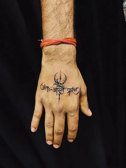 Hand tattoos make a bold statement, and we ensure they are clean and powerful. This piece features the Sanskrit shloka 'Ant asti prarambh' (the end is the beginning) combined with a Trishul, creating a striking symbol of life's cyclical nature right on the hand.