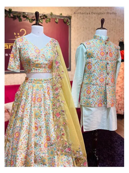 This coordinated couple set is perfect for sangeet or engagement ceremonies. It includes an off-white lehenga with vibrant multi-color floral embroidery, paired with a mint-green kurta and a matching embroidered Nehru jacket.