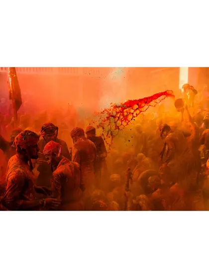 A stream of red liquid color is thrown through a cloud of orange powder during Holi. This action shot freezes a dynamic and beautiful moment of celebration.