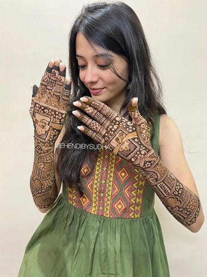 A happy bride showing off her intricate bridal mehendi, which includes figures, symbols, and beautiful check patterns.