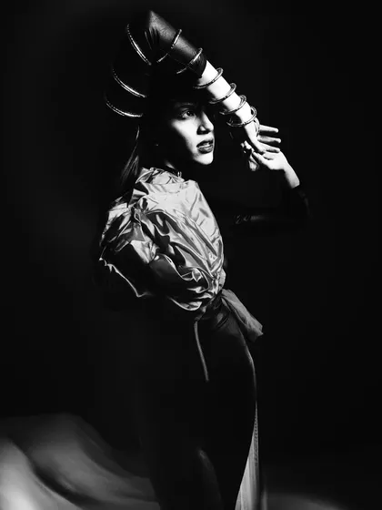 A black and white shot from the same series, emphasizing the dramatic shapes of the headpiece and the flowing fabric. The high contrast creates a timeless, sculptural feel.