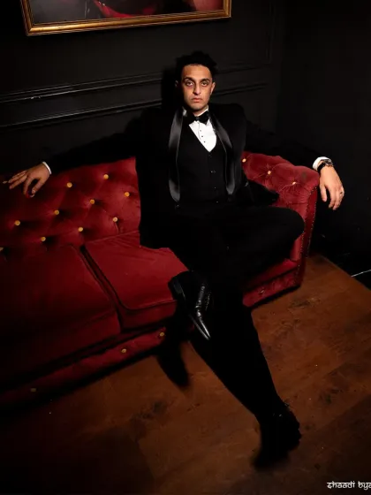 A dapper groom's portrait. The dark, moody lighting and the confident pose on the red sofa create a very stylish, editorial feel.