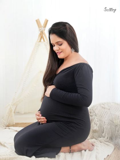 A serene portrait of a mother-to-be in a black dress against a boho-inspired backdrop. The contrast between the dark dress and the light, airy setting creates a beautiful and unique look.