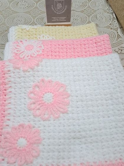I offer these baby blankets in various colors. Here you can see the pink and white version next to a yellow and white one, both featuring the same floral design.