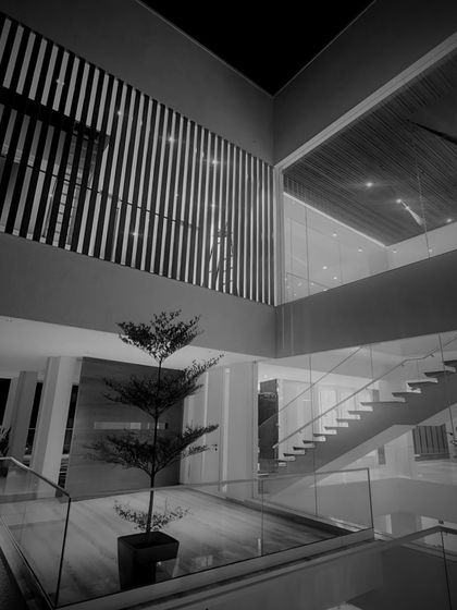 A black and white shot emphasizing the clean lines and geometric purity of this interior. The floating staircase, glass railings, and double-height space create a composition of minimalist elegance.