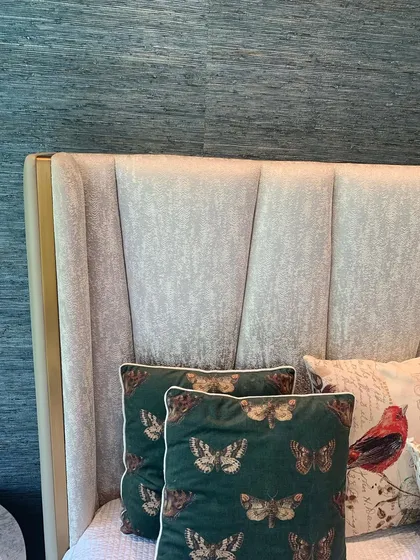 A close-up of a headboard with custom upholstery, set against a textured wallpaper. The butterfly-print cushions add a touch of whimsy.