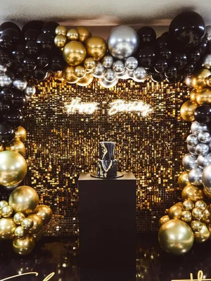 You can never go wrong with a bit of sparkle. This glamorous birthday backdrop features a shimmering gold sequin wall, a custom 'Happy Birthday' neon sign, and a dramatic balloon arch in black, gold, and silver. It’s designed to make a statement.