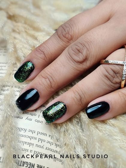 A daring and dazzling design featuring black nails with a captivating green flakes glitter effect on the accent nails. This look is perfect for those who want to make a bold statement.