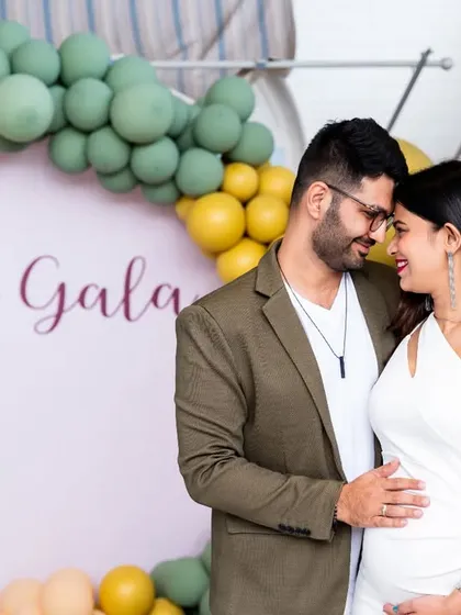 An elegant portrait of an expecting couple at their baby shower, sharing an intimate moment in front of a stylish balloon decoration.