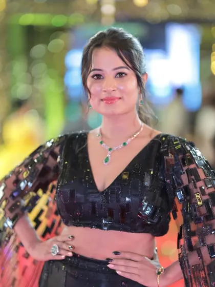 A portrait of Anusha Rai, focusing on her beautiful emerald necklace that complements her black outfit.