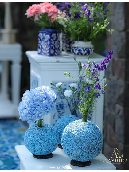 A unique decor detail featuring handwoven powder-blue thread vases holding delicate flowers, adding a touch of craft and color to the tables.