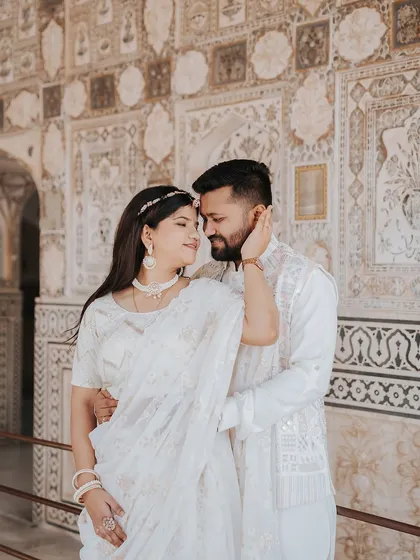A tender moment captured against the detailed walls of Amer Fort, with the bride gently touching the groom's face.
