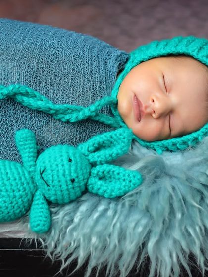 So tiny and sweet. This newborn is swaddled in a knitted turquoise wrap with a matching bunny-eared bonnet and a little toy, sleeping peacefully on a soft fur blanket.