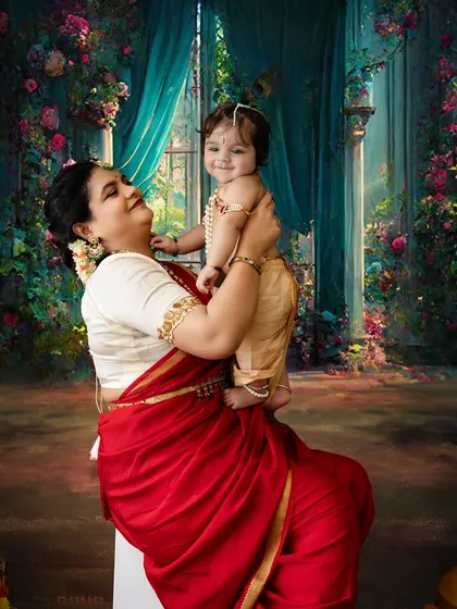 A magical moment as a mother lifts her smiling baby Krishna. The ornate, floral backdrop adds a touch of fantasy and beauty to this special photoshoot.