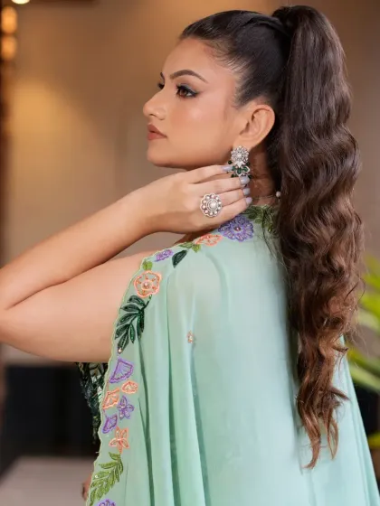 A side profile showcasing the elegant high ponytail and floral embroidered cape of the pastel green lehenga. The matching earrings add a perfect finishing touch.