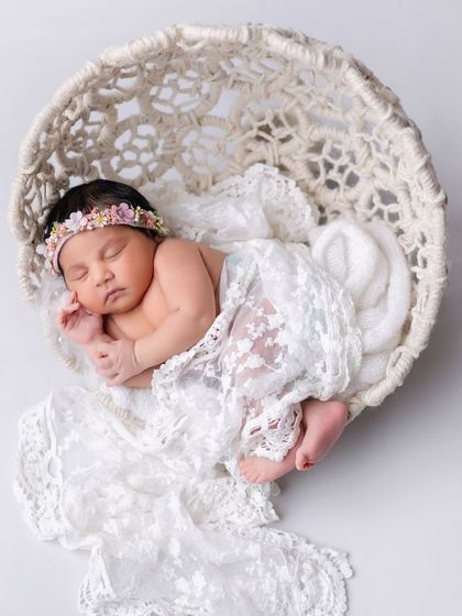 A delicate newborn portrait. The baby is sleeping peacefully in a woven basket, draped in beautiful white lace.