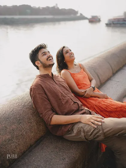 Pure joy captured in a candid moment. Nikit and Anusha look up at the sky, laughing together by the water, showing the simple happiness that defines their relationship.