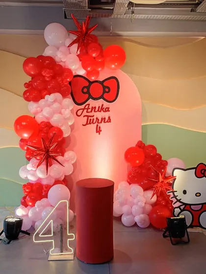 A clean and modern Hello Kitty theme for a 4th birthday. This setup includes a custom arched backdrop with the birthday girl's name, a Hello Kitty cutout, a light-up number '4', and a vibrant red and white balloon garland.