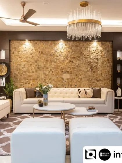 This luxurious living room features a stunning accent wall with natural stone cladding. The neutral tufted sofas, elegant chandelier, and marble coffee tables come together to create a space that is both grand and welcoming.