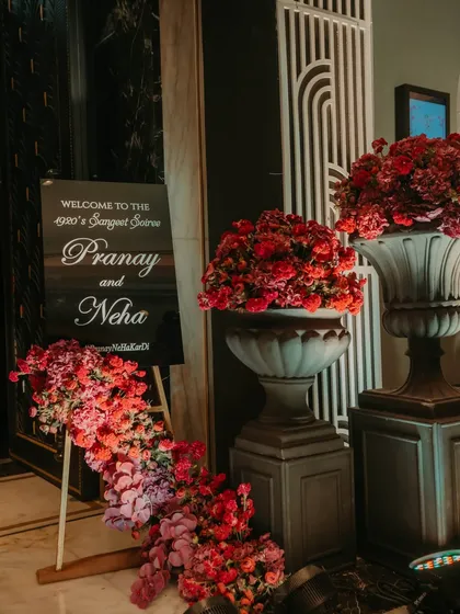 The welcome signage for the "1920's Sangeet Soiree," flanked by dramatic red floral arrangements, setting the tone for a night of vintage glamour.