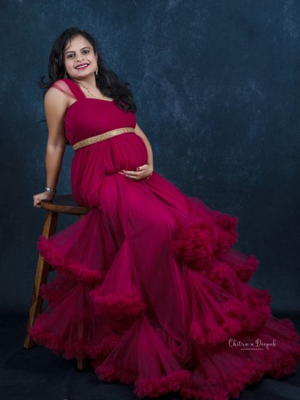 Seated gracefully in a magenta ruffled gown. This pose is comfortable for moms-to-be and beautifully showcases the dress's texture and color.