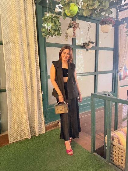 A full-length view of the all-black ensemble. The combination of a structured waistcoat and a flowy skirt creates a beautiful contrast in textures and silhouettes, resulting in a sophisticated and modern look.