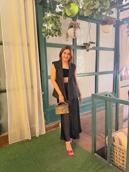 A full-length view of the all-black ensemble. The combination of a structured waistcoat and a flowy skirt creates a beautiful contrast in textures and silhouettes, resulting in a sophisticated and modern look.