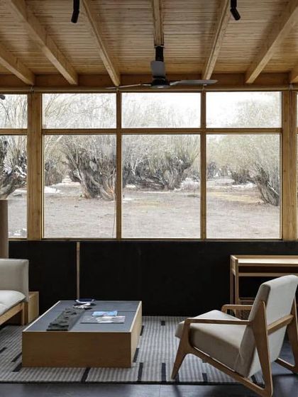 The Postcard in the Himalayan Willows by A L V A architects, a WAF finalist. This interior view shows a serene living space with large windows framing the starkly beautiful high-altitude desert landscape of Ladakh.