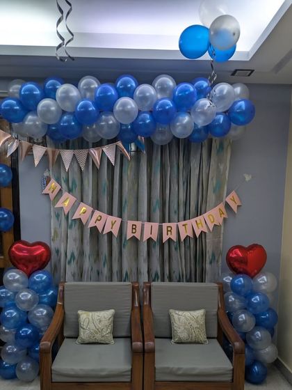 A simple and classic living room setup with a blue and silver balloon arch over the seating area and a "Happy Birthday" banner.