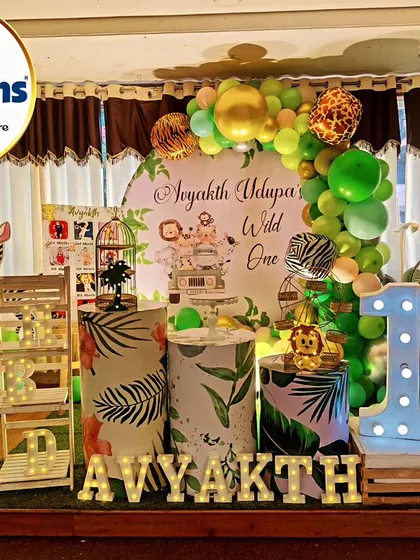 A complete jungle-themed setup for a "Wild One" first birthday. The decor features a circular backdrop, animal cutouts, and a large light-up number '1'.