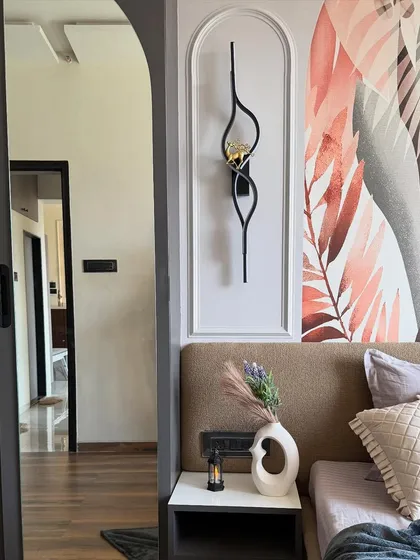 A view of the master bedroom's bedside, showing the artistic wall sconce, a large arched mirror, and a statement wallpaper with a botanical theme.