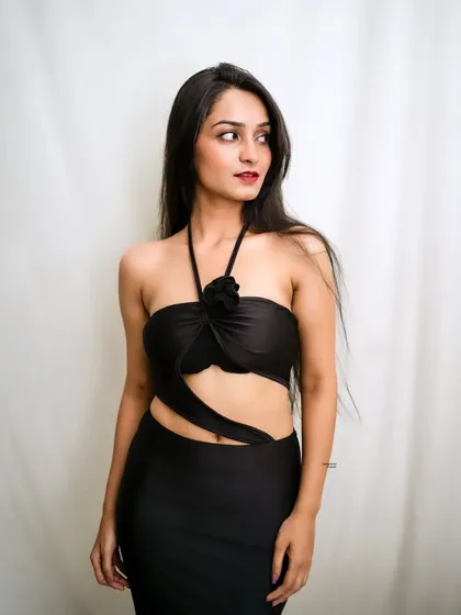 A stylish portrait of a model in a black cutout dress with a floral detail, looking off to the side with a confident expression.