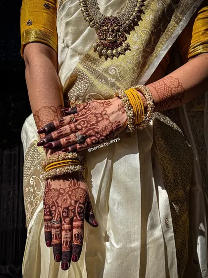 A stunning photo of a bride in a traditional South Indian saree, showcasing her beautifully stained mehendi. The dark henna provides a gorgeous contrast against her elegant attire.