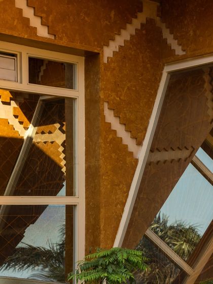 The stone-resin pattern is reflected in the angled window, demonstrating how the facade's geometry interacts with every element of the building.