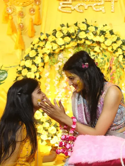 Sisters sharing a playful moment, smearing haldi on each other against the festive decor. Capturing these candid family moments is a core part of our wedding photography service.