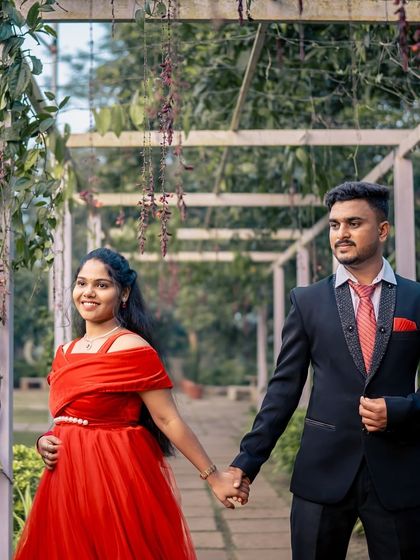 A happy couple walking hand-in-hand during their pre-wedding shoot. The bright red off-shoulder gown is a classic choice for a romantic and vibrant look.