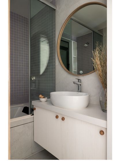 The kids' bath in the Noir Blanc House features lavender piccolo square tiles highlighting the bathtub area. A wooden mirror and fluted vanity enhance the space, which also includes a jacuzzi for a touch of fun luxury.