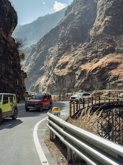 A line of SUVs, including a Jimny and a Ford, crosses a bridge on a mountain road, demonstrating my ability to capture multiple vehicles in a dynamic, scenic setting. The composition highlights the scale of the journey.