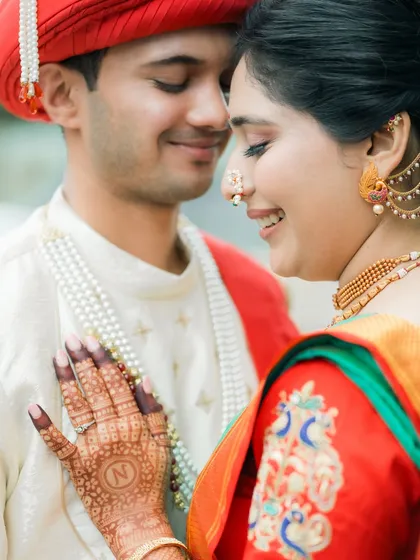 A close-up shot highlighting the bride's hand with an 'N' initial in her mehndi, resting gently on the groom's chest. A sweet, personal detail.