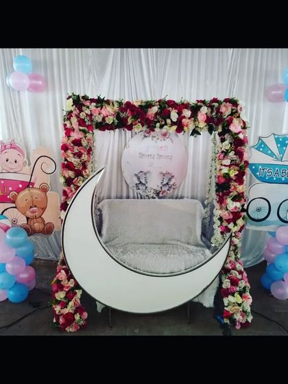 A clean and elegant baby shower setup with a white moon prop and a floral swing. The pink and blue cutouts on either side add a pop of color.