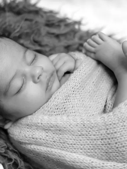 A close-up black and white shot of a swaddled newborn, focusing on their tiny feet and peaceful sleep. These detail shots are a client favorite.