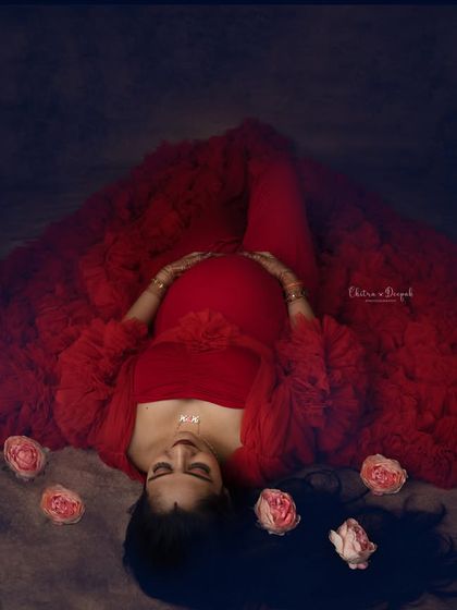 A creative top-down shot creating a heart shape with the dramatic red gown. This artistic angle offers a unique and memorable maternity portrait.