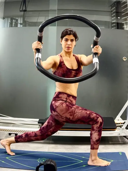 A client performs a lunge with a magic circle, a prop that adds resistance and helps to engage the inner and outer thighs. This variation intensifies the exercise and improves muscle activation.