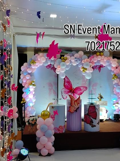 A dreamy butterfly stage decoration with hanging butterfly strands and fairy lights. The pastel balloon arch and themed props create a truly enchanting atmosphere.